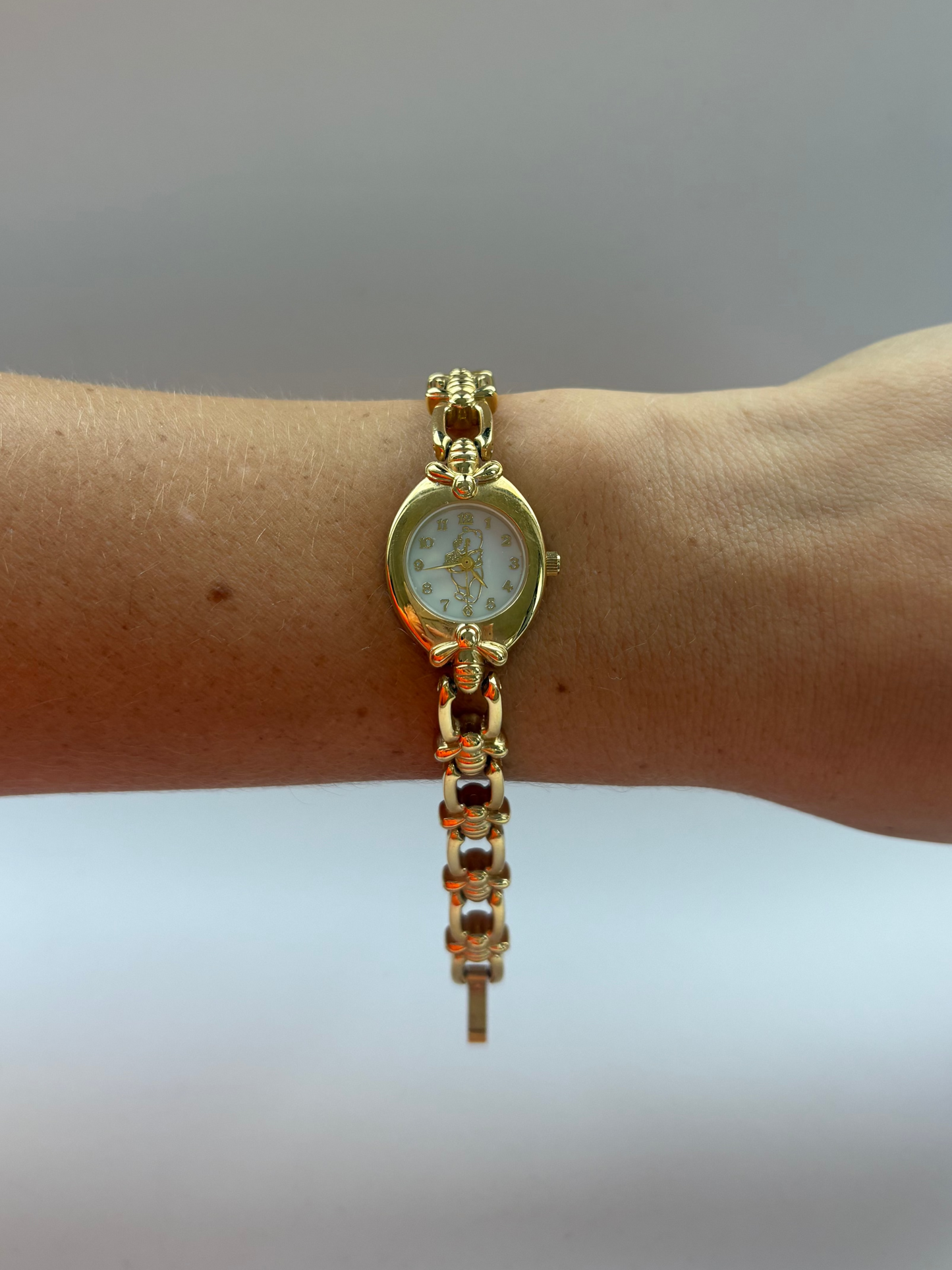 Gold wristwatch on a wrist with a plain background